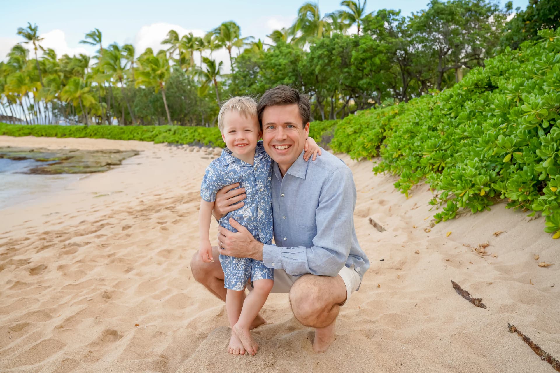 Father and young son hugging on the beach in matching aloha outfits
