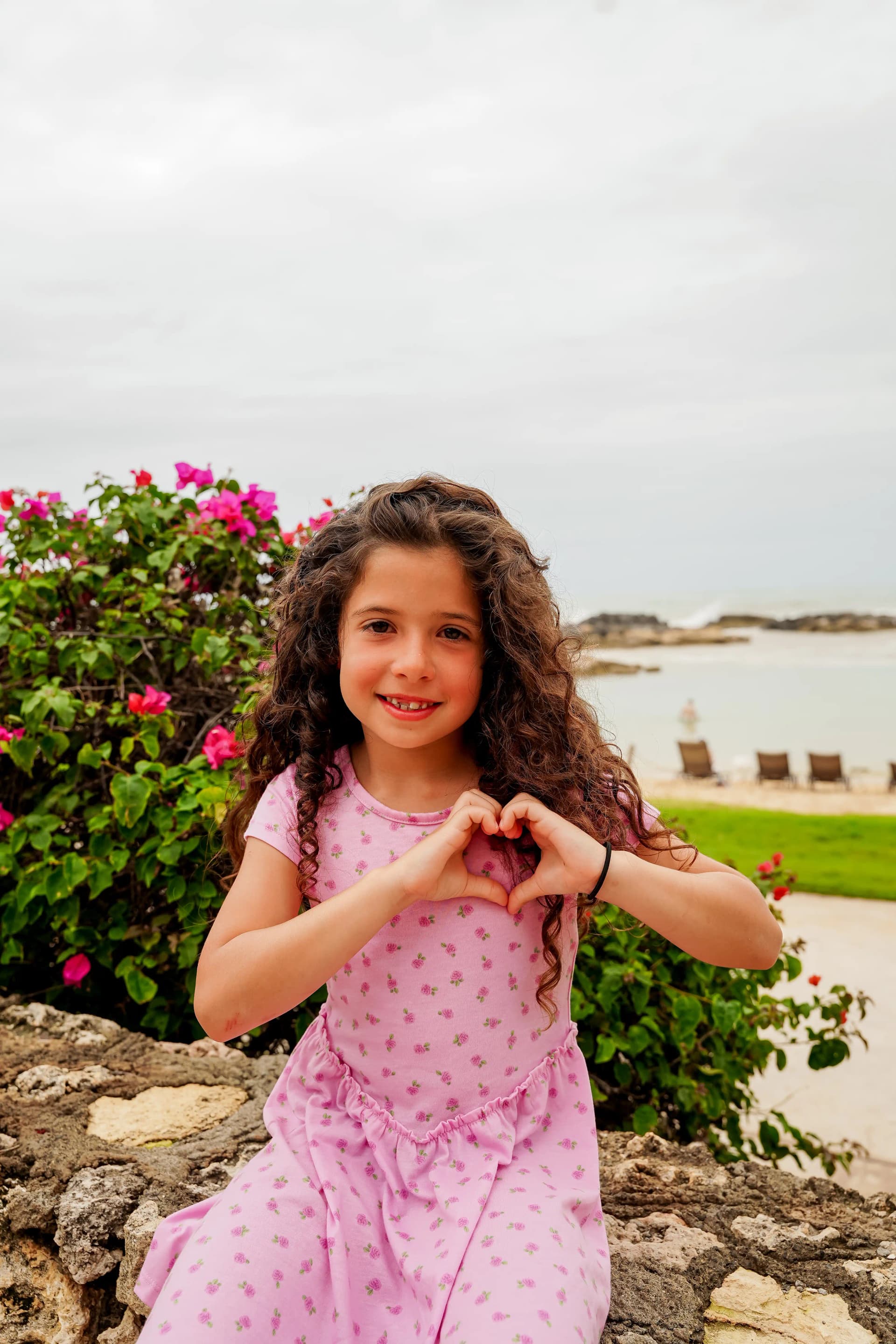 Young girl solo portrait with curly hair and heart hands by the ocean