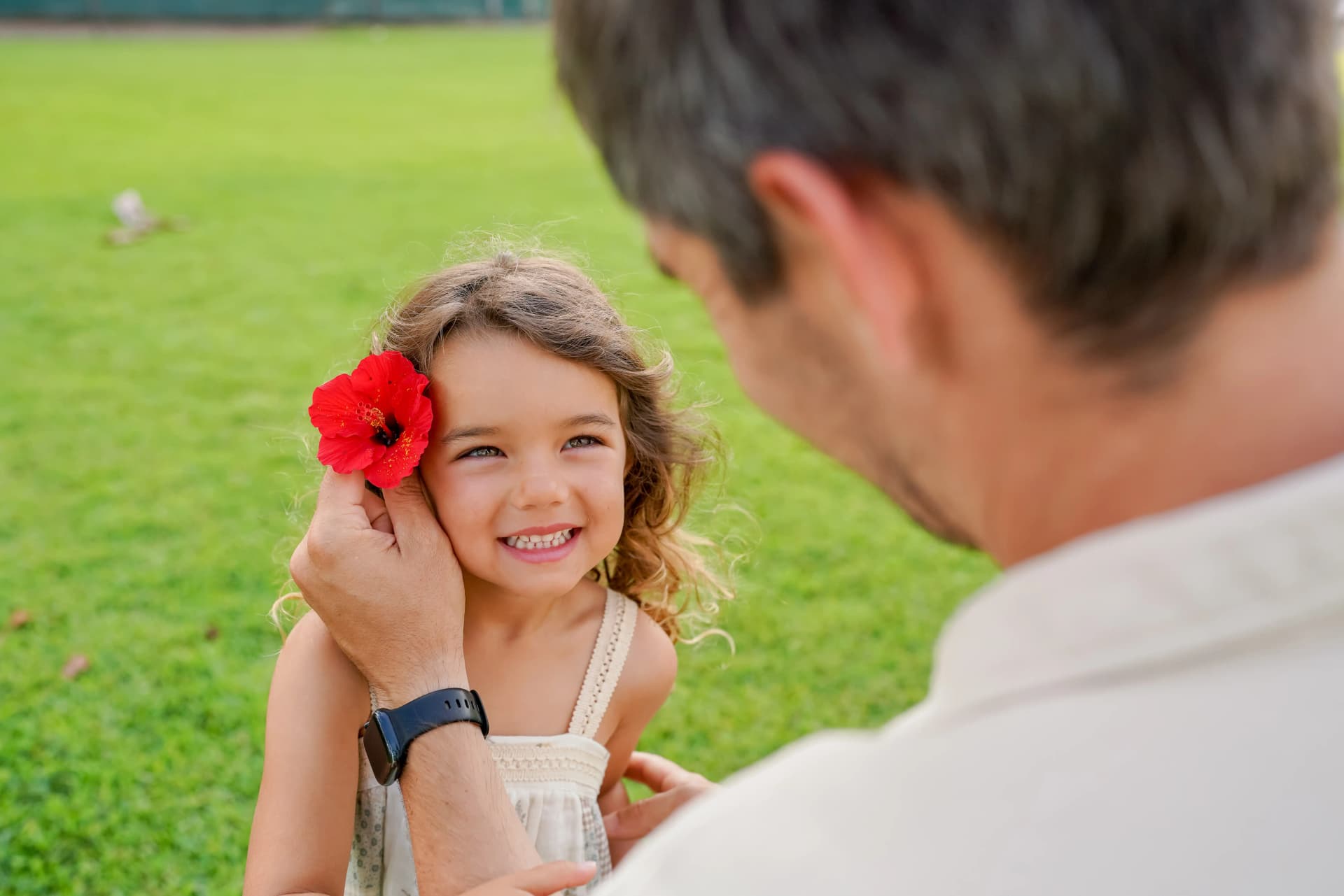 Father placing hibiscus flower on little girl's hair in garden